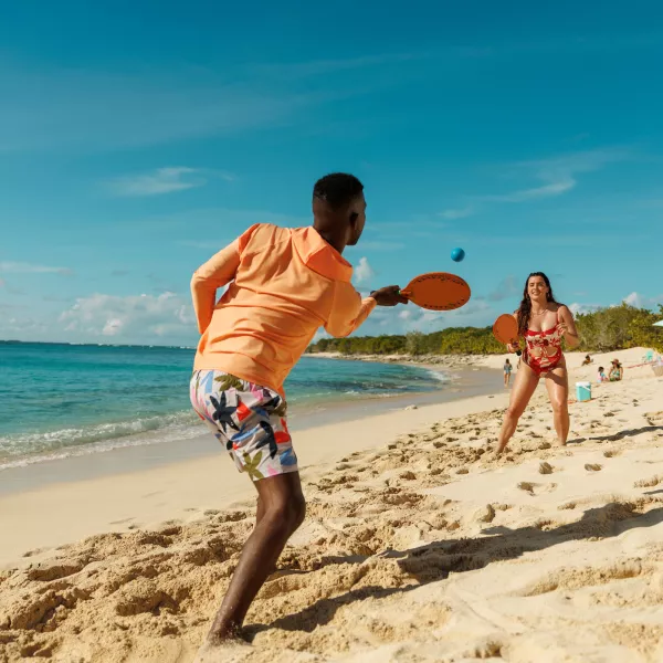 Two people playing paddle ball on a sandy beach in Puerto Rico, with turquoise water, clear blue skies, and tropical scenery in the background.