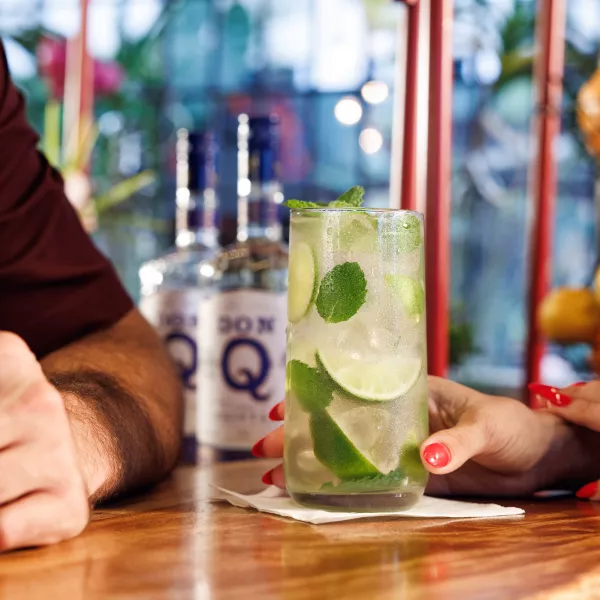 Close-up of a rum cocktail with lime and mint on a bar counter in Puerto Rico, with fresh citrus and liquor bottles blurred in the background.