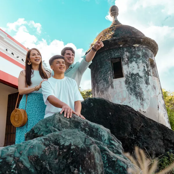 A family of three people standing at the front of a Garita while the dad is pointing at the horizon.