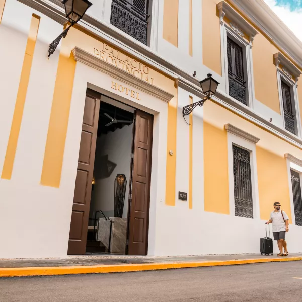 Two travelers walking with luggage outside a historic hotel in Old San Juan, Puerto Rico.