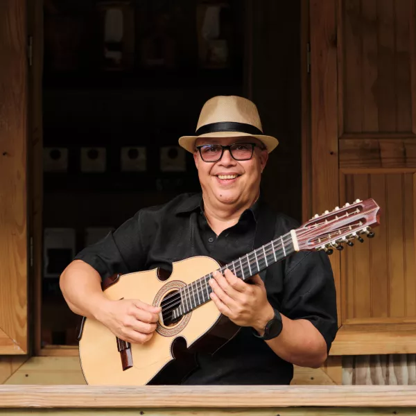 A guitarist holding his instrument with a bright smile on his face wearing a hat.
