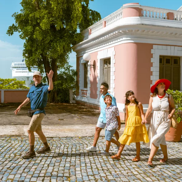 A family of four is walking through el Viejo San Juan with their tour guide signaling a structure.