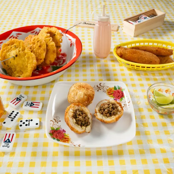Tres comidas fritas encima de una mesa, acompañada de vinagre, mayoketchup, limón y dominos.