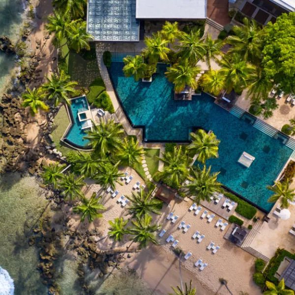 Aerial view of Dorado Beach, a Ritz-Carlton Reserve, featuring oceanfront pools, palm trees, lounge chairs, and a sandy beach along Puerto Rico's coast.