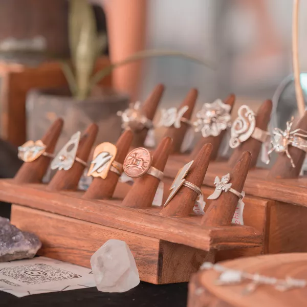 Anillos artesanales con diseños inspirados en la naturaleza y expresiones artísticas exhibidos en un soporte de madera durante una feria artesanal en Puerto Rico.
