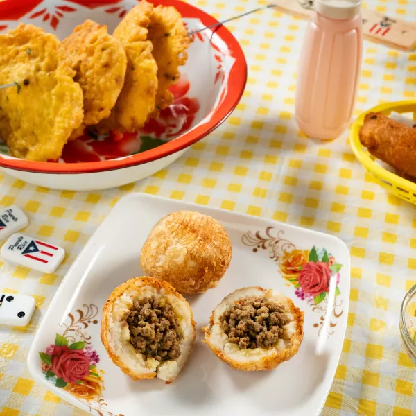 A variety of Puerto Rican fritters, including alcapurrias and rellenos de papa, served on a checkered tablecloth in Piñones, a destination known for its roadside kiosks and fried snacks.