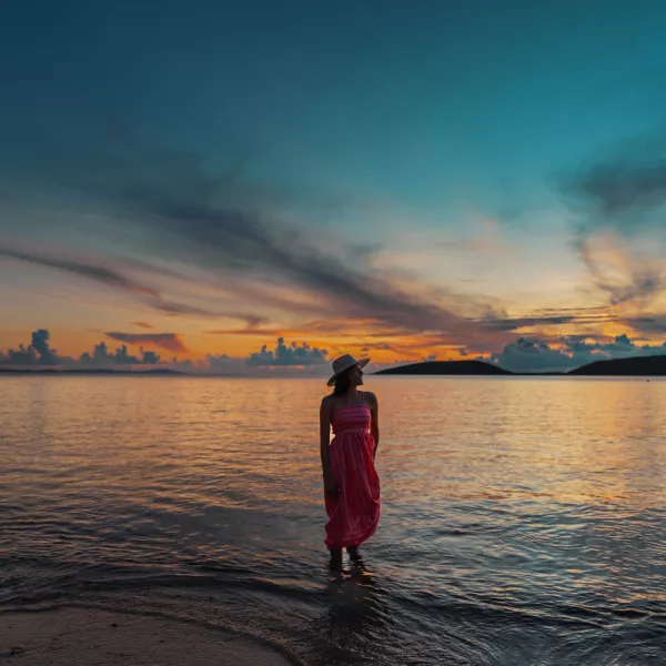 Woman standing in shallow water at sunset in Culebra, Puerto Rico, with colorful skies reflecting across the calm sea.