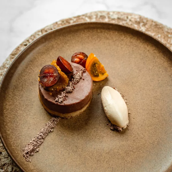A beautifully plated chocolate dessert topped with roasted grapes and fruit, served with a quenelle of cream on a minimalist ceramic plate at Cocina Abierta.