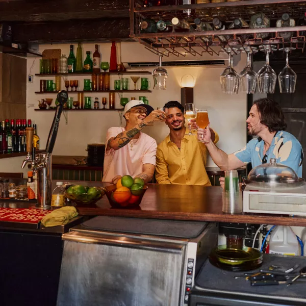 Three friends raise glasses for a toast at a cozy bar in Puerto Rico, enjoying local craft beer and drinks in a warm, inviting setting.