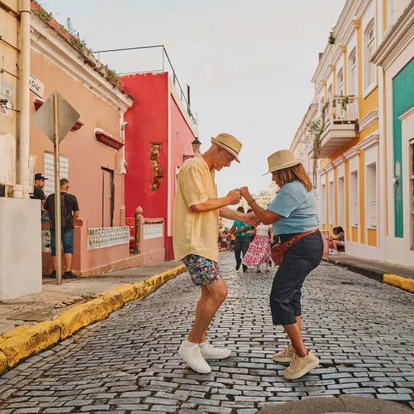A couple dances on a cobblestone street in Old San Juan, Puerto Rico, surrounded by colorful colonial buildings during a lively day of exploring the historic city.