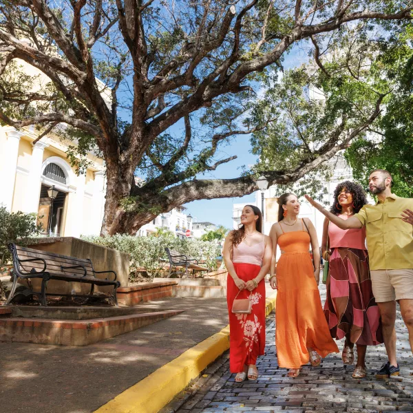 3 travelers and 1 tour guide walk along a cobblestone street in Old San Juan, Puerto Rico, admiring the historic architecture and lush trees while exploring the city's colorful, walkable neighborhood.