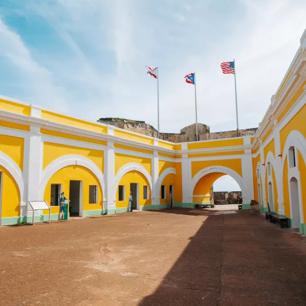 Interior courtyard of El Morro in Old San Juan, featuring historic yellow arches, three flags, and the fortress's preserved military architecture.