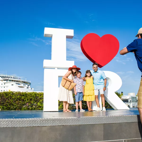 Family posing in front of the I Love Puerto Rico sign in Old San Juan with a cruise ship visible in the background.
