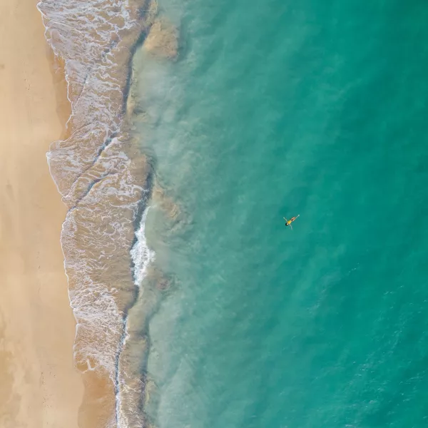 Aerial view of a swimmer floating in clear turquoise water beside a sandy beach in Puerto Rico.