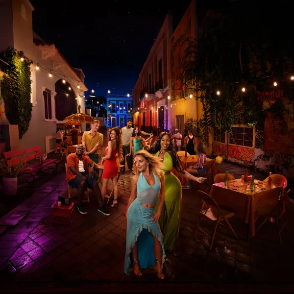 Cast members from TLC’s 90 Day: Hunt for Love pose on a colorful, mural-lined street in Puerto Rico at night, surrounded by café tables and string lights.