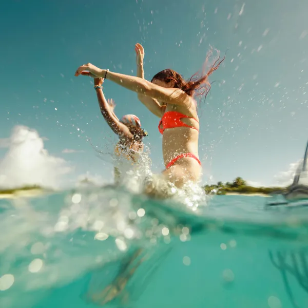 Two people jump into clear turquoise water at Icacos, with a boat ladder visible on the right.