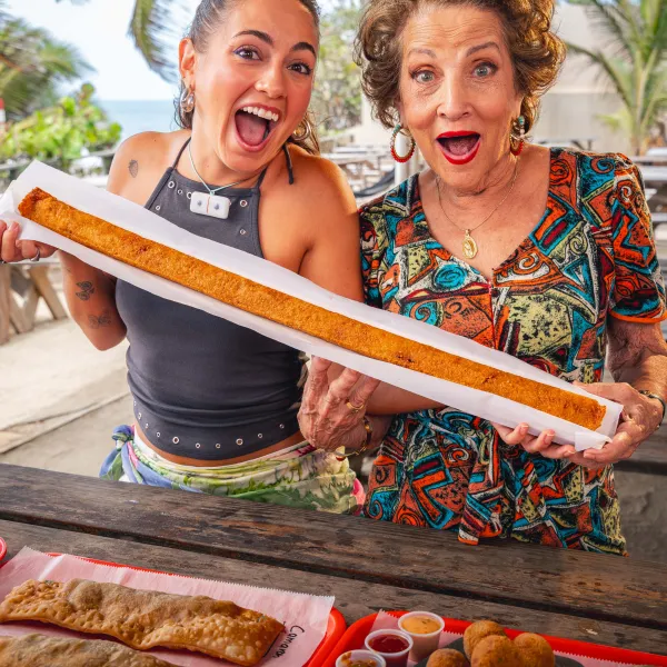 Sabor del Pueblo hosts excitedly hold an extra-long alcapurria at an outdoor restaurant in Guayama.