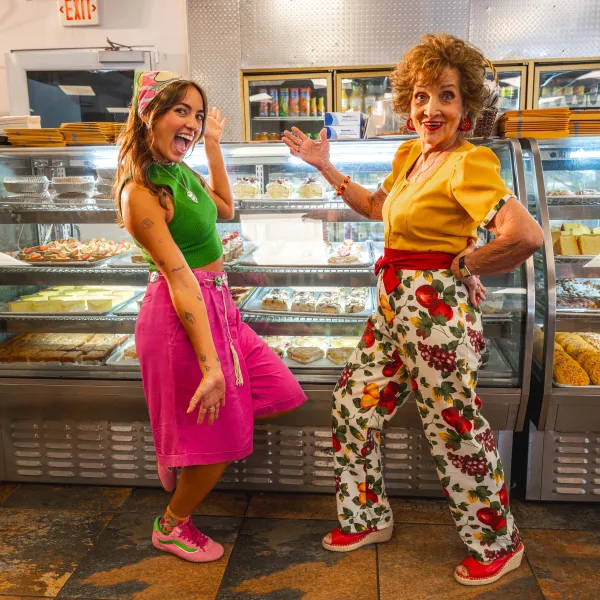 Sabor del Pueblo hosts pose playfully in front of a bakery display filled with pastries in Mayagüez, Puerto Rico.