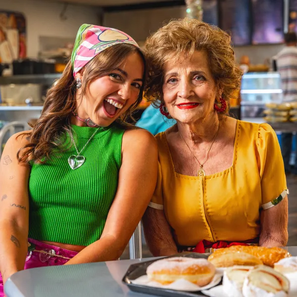 Sabor del Pueblo hosts Bianca Montoya and her abuela, María Legrand, smile together beside a tray of pastries in Mayagüez, Puerto Rico.