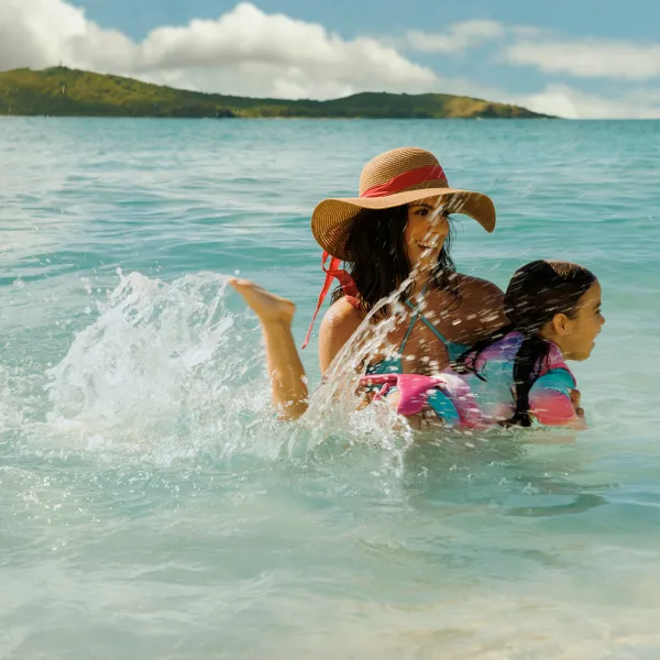 A female traveler with her kid enjoying the shallow turquoise waters of Cayo Icacos near Fajardo, with calm Caribbean seas, a sandy shoreline, and green hills in the distance.