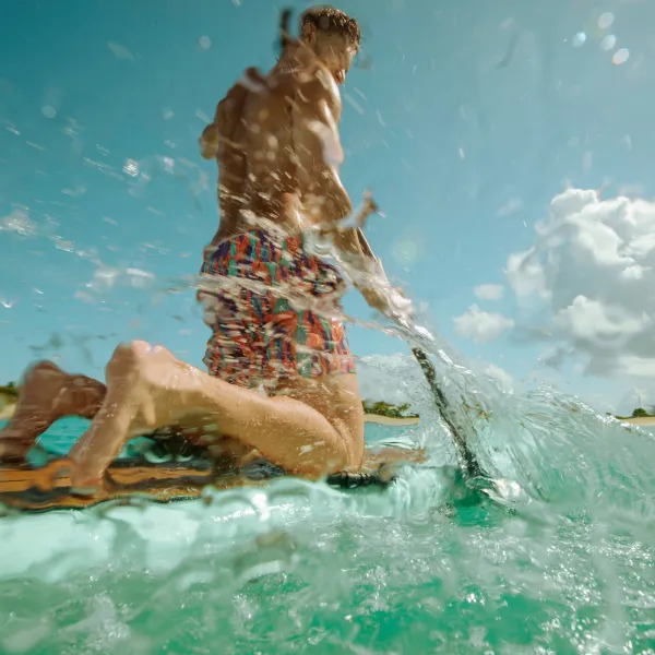 Visitor kneeling in the crystal-clear waters of Cayo Icacos, with turquoise waves, white-sand shoreline, and a bright Caribbean sky in the background.