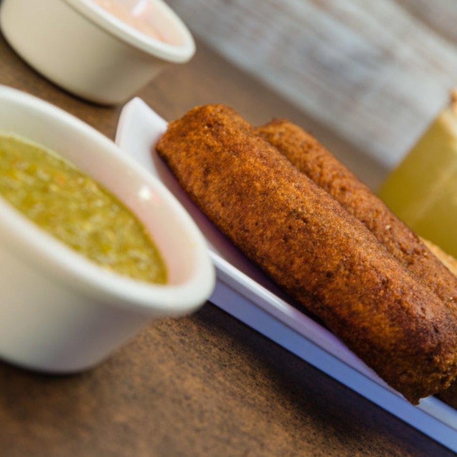 A plate of alcapurria fritters with a bowl of green sauce.
