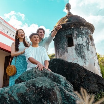 A family of three people standing at the front of a Garita while the dad is pointing at the horizon.