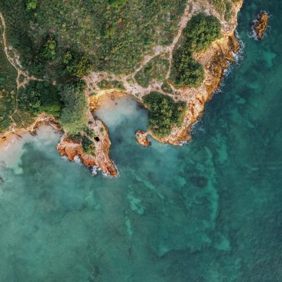 Vista aérea desde un ángulo alto de una costa escarpada en Puerto Rico, con acantilados dorados y vegetación exuberante que se encuentran con las cristalinas aguas turquesas de Cabo Rojo.