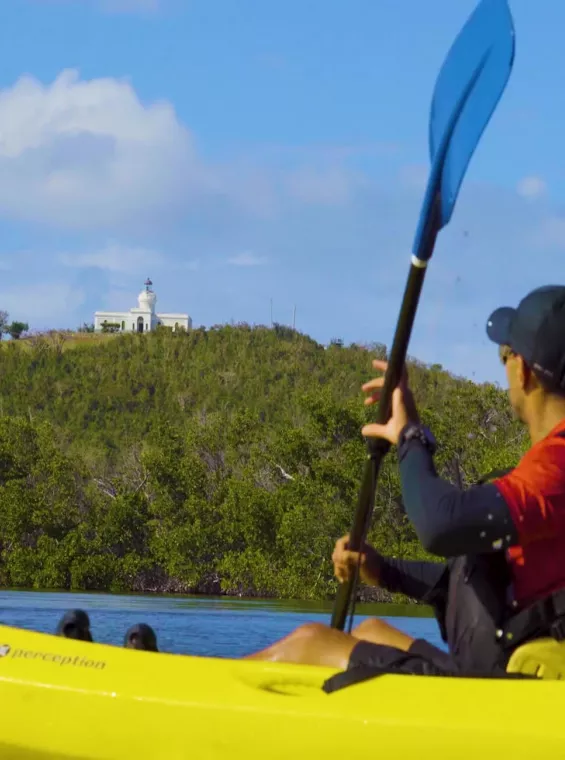 Kayakista remando por el Parque Las Croabas y el Faro de Fajardo, el faro más antiguo de Puerto Rico.