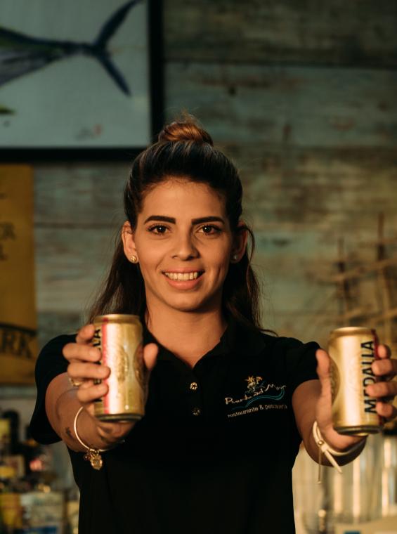 A bartender in San Juan holding two cans of Medalla.