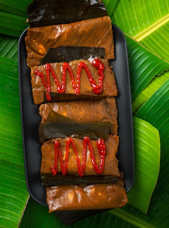 Plate of pasteles with and without ketchup on top of banana leaves.