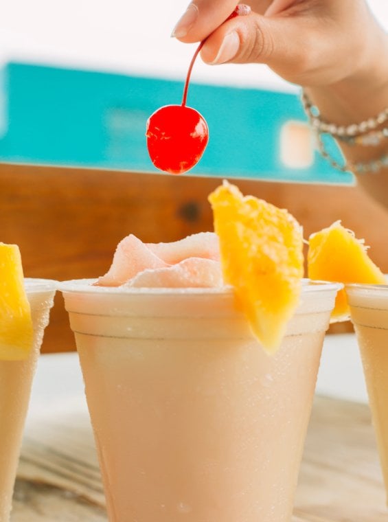 A frozen cocktail is garnished with maraschino cherries and fresh pineapple slices.