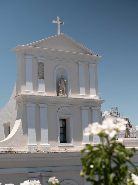 Exterior of Catedral de San Juan Bautista in San Juan, Puerto Rico, with a white flowering tree in the foreground.