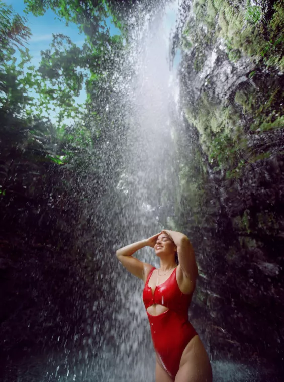 Woman standing under a waterfall in El Yunque rainforest with water cascading down around her.